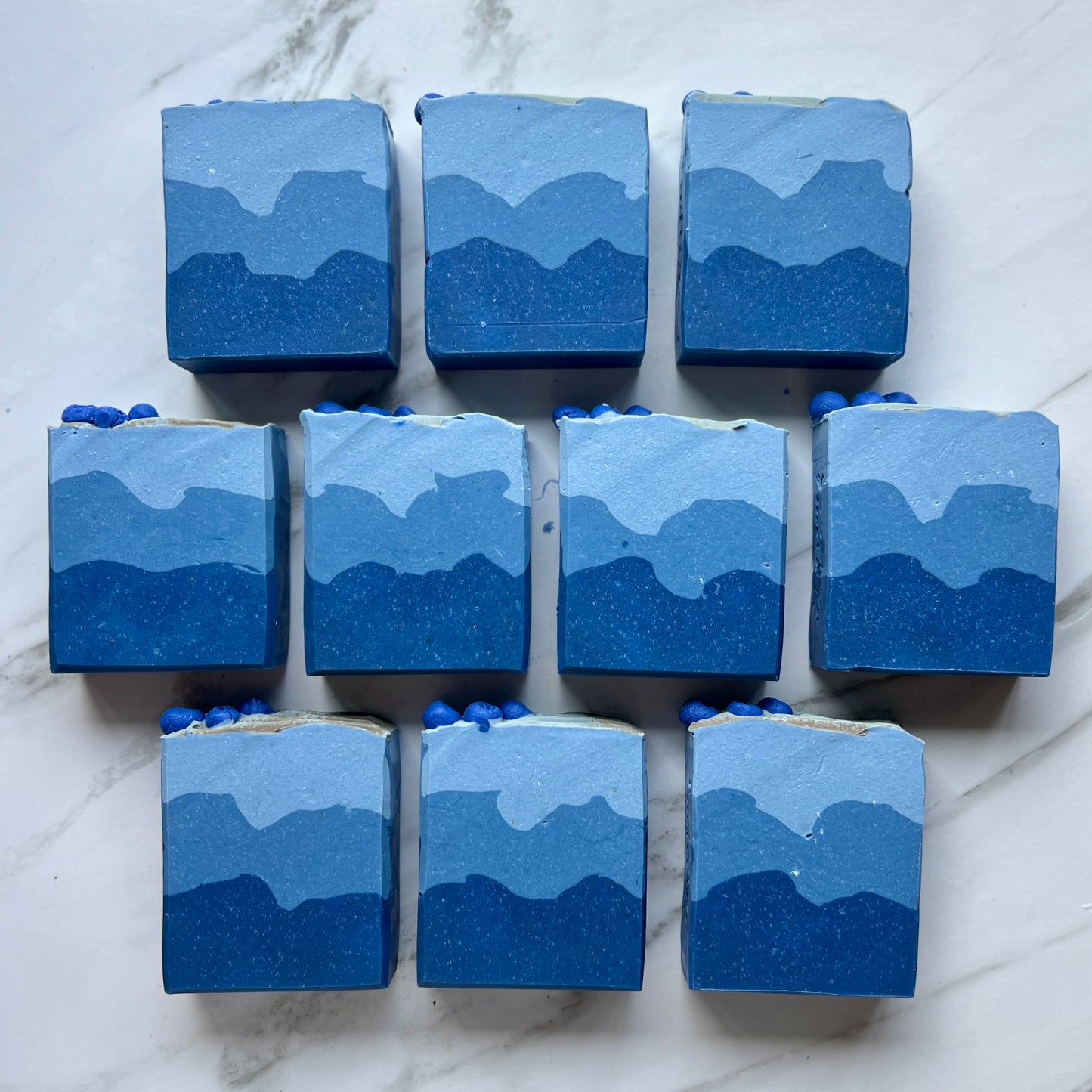 Handmade soap on a countertop showing the front of the soap. Blue soap with three layers. Dark blue on the bottom, a lighter shade in the middle, and the lightest blue on top.