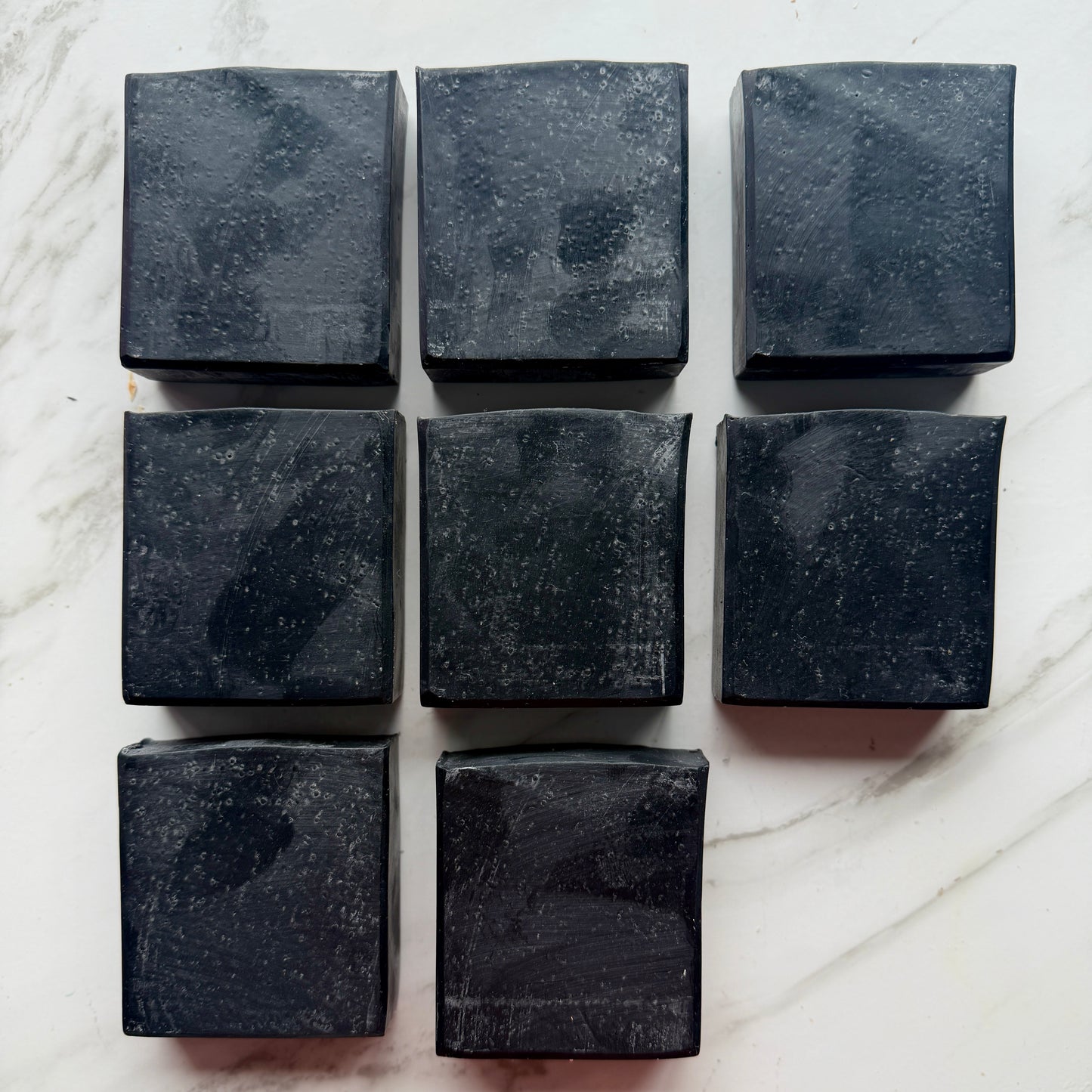 Eight rectangular dark charcoal soap bars arranged in a grid on a white marble surface.
