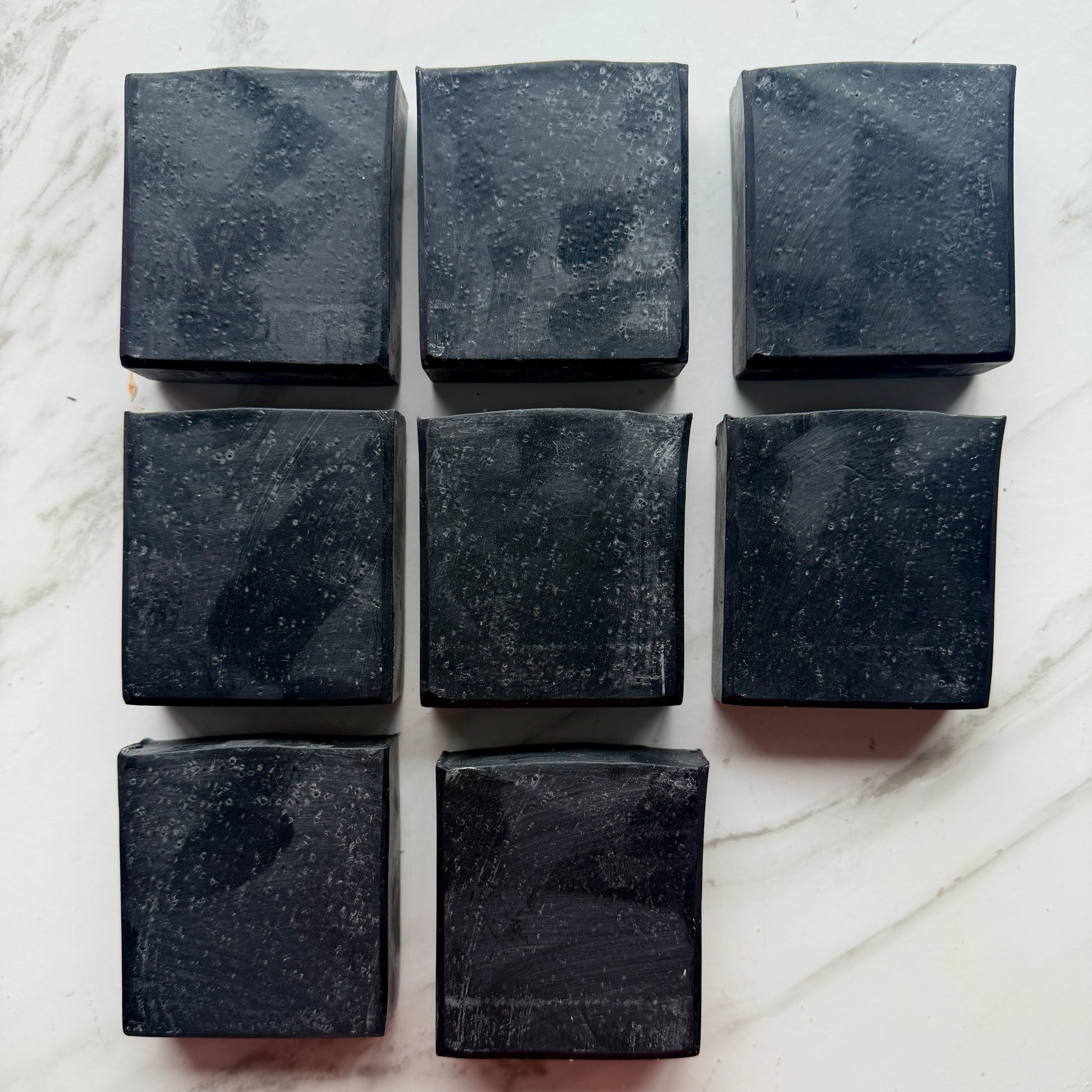 Eight rectangular dark charcoal soap bars arranged in a grid on a white marble surface.